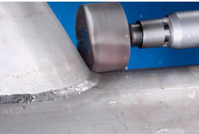 Ein Metallschneideisen bei der Arbeit, das die Kante eines metallischen Kegels vor blauem Hintergrund trimmt und dabei präzises, glattes Schneiden demonstriert.