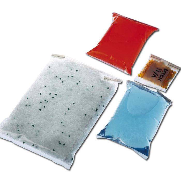 Vier versiegelte Kunststoffbeutel mit farbigen Trockenmittelpäckchen: ein großer weißer Beutel gefüllt mit Kügelchen, ein roter Beutel, ein blauer Beutel und ein kleines beschriftetes Päckchen.