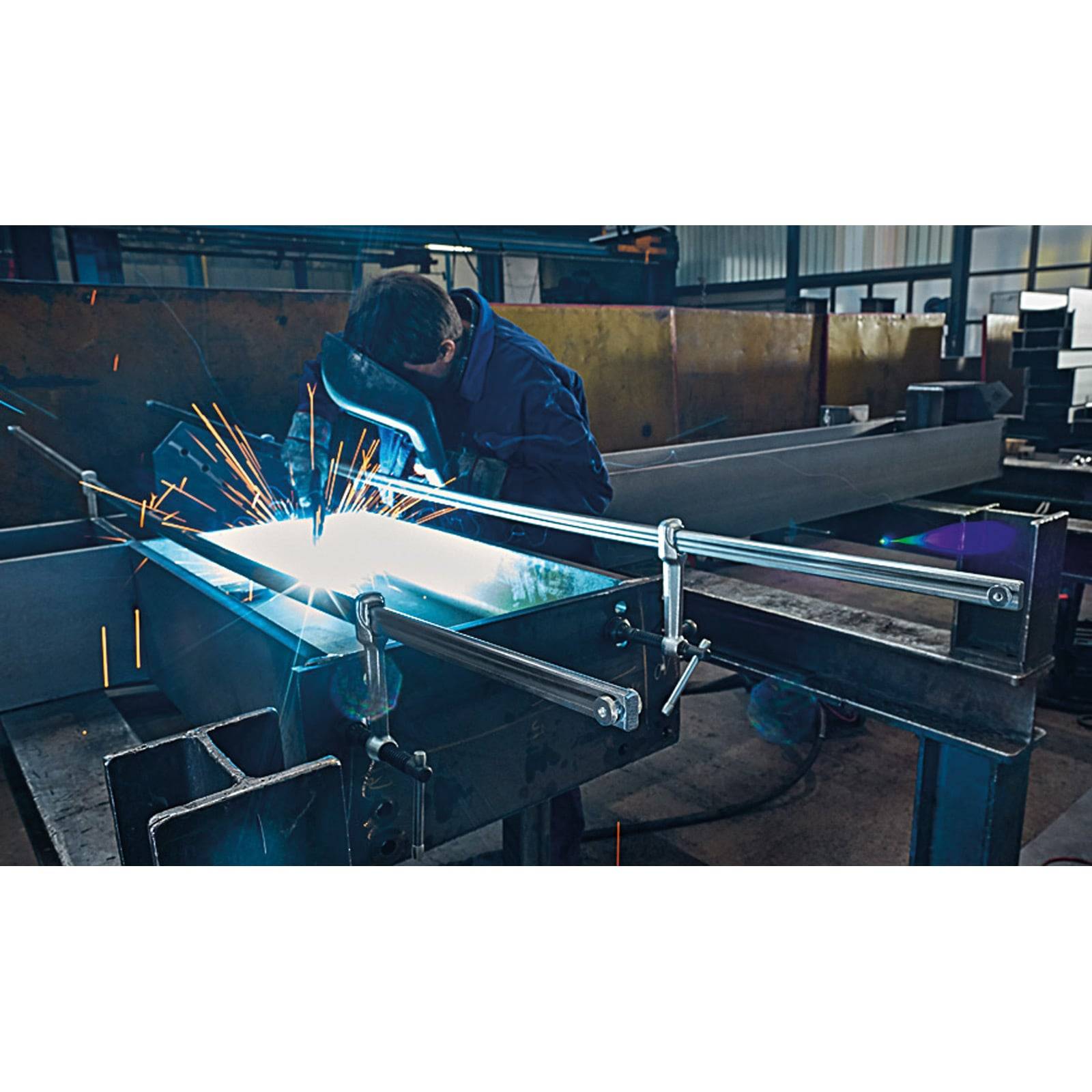 Ein Arbeiter in Schutzausrüstung schweißt Metallträger und erzeugt helle Funken in einer Fabrikhalle. Die Umgebung ist industriell mit verschiedenen Ausrüstungsgegenständen.