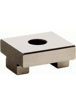 Ein rechteckiger Metallblock mit einem zentralen kreisrunden Loch sitzt auf einem kleinen Sockel erhöht. Die Oberfläche ist reflektierend und glatt.