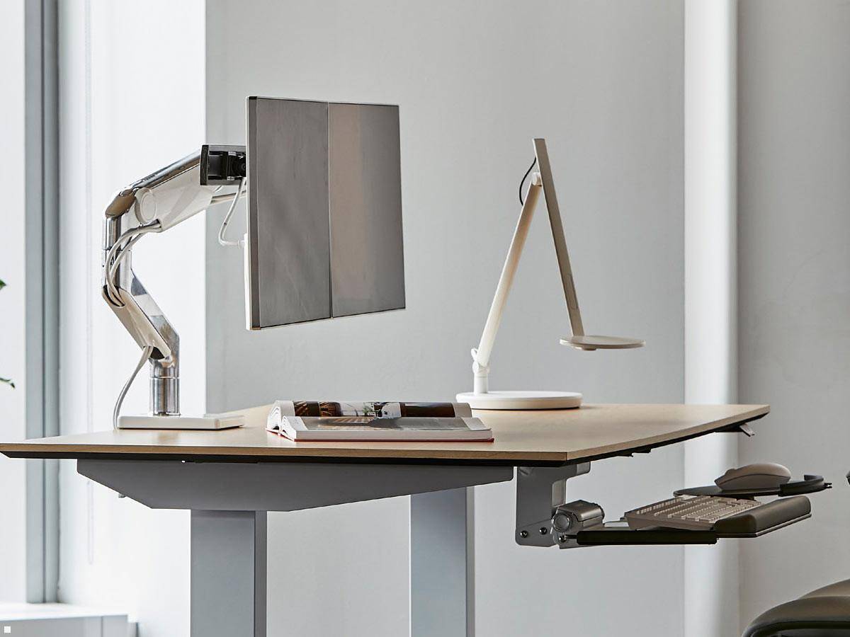 Ein verstellbarer Stehschreibtisch mit zwei Monitoren, Tastatur, Maus und Bürostuhl, der in einer sauberen, modernen Arbeitsumgebung platziert ist.