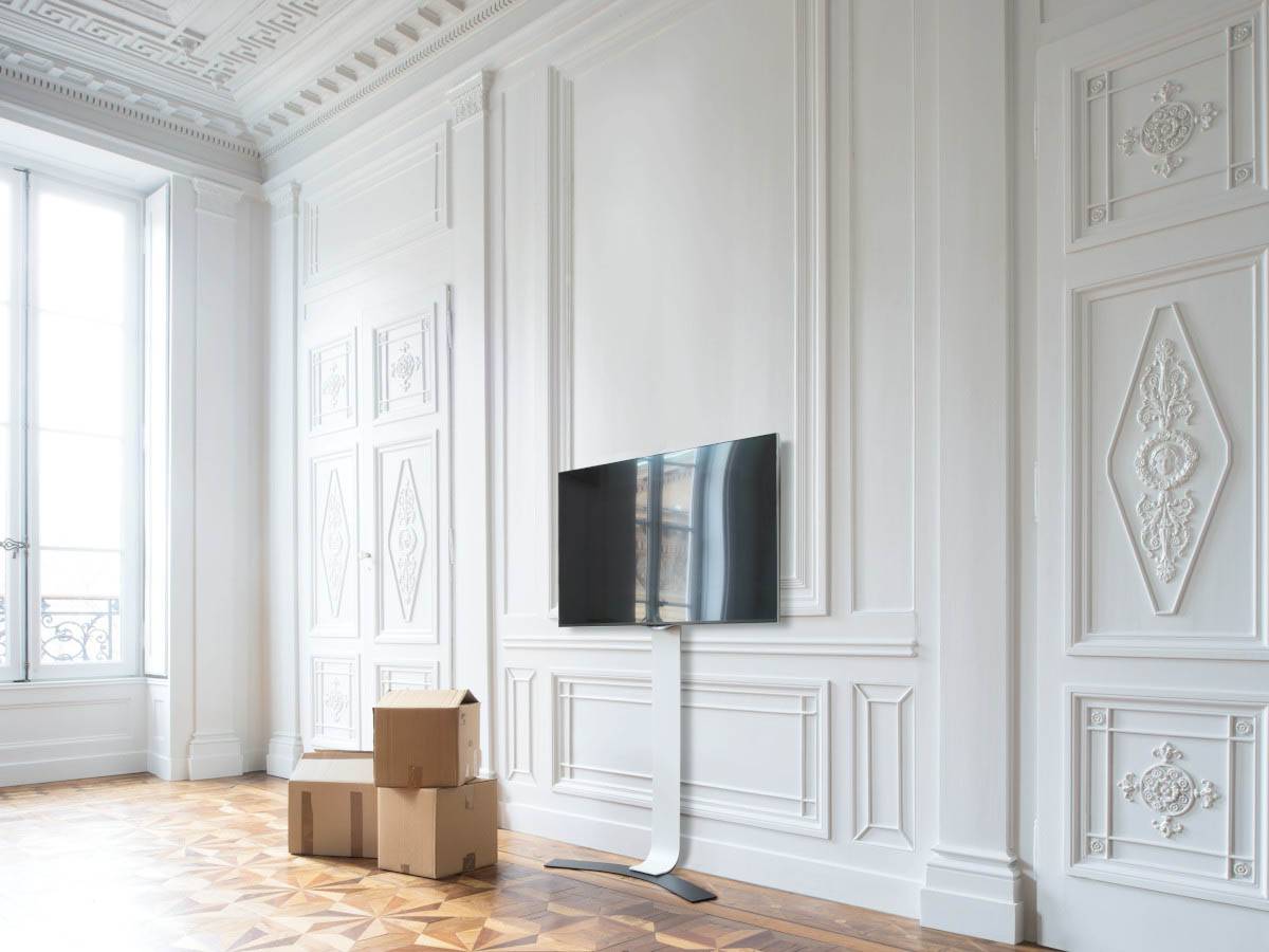 Leerer eleganter Raum mit kunstvoll gestalteten weißen Wänden und Decke, Holzparkett-Böden, drei Kartons und einem schlanken Fernseher auf einem Ständer.