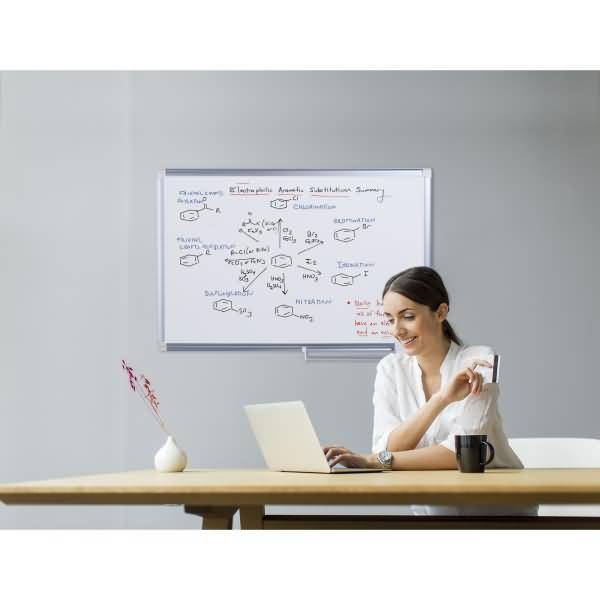 Frau, die an einem Laptop neben einem Whiteboard mit Chemienotizen und Moleküldiagrammen in einem minimalistischen Büro arbeitet.