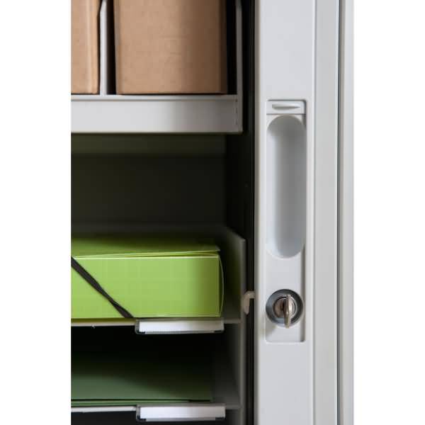Offener Schrank mit Regalen, die Kartonboxen und eine grüne Lagerkiste mit schwarzem Riemen halten, aus nächster Nähe von der Seite betrachtet.