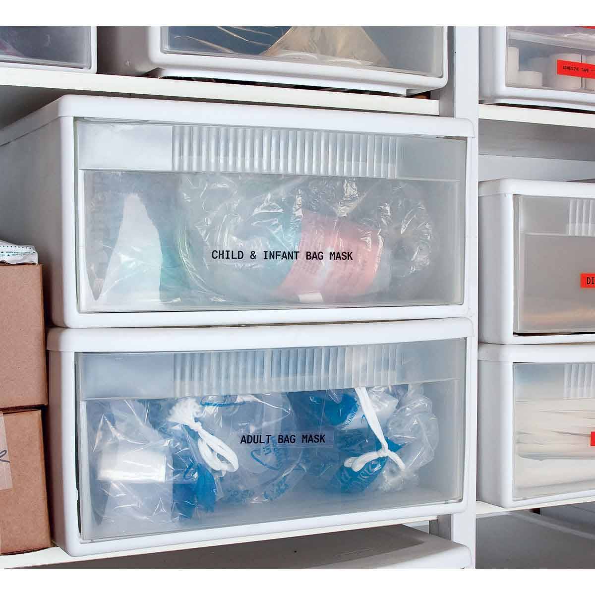 Gestapelte transparente Lagerschubladen mit den Etiketten 'CHILD & INFANT BAG MASK' und 'ADULT BAG MASK' mit verpackten Masken.