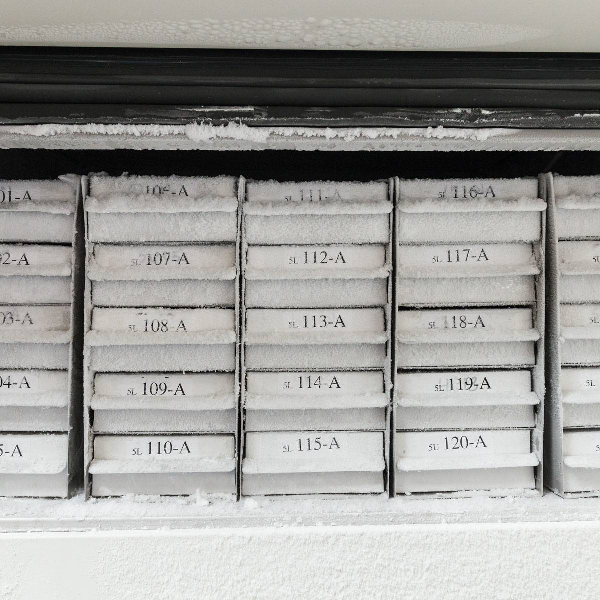 Reihe von frostigen nummerierten Briefkästen oder Lagerfächern mit den Etiketten 107-A bis 120-A hinter einer kalten, weißen Türplatte.