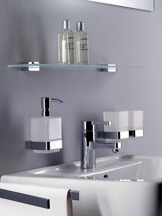 Ein minimalistisches Waschbecken mit Chrom-Armatur, wandmontiertem Seifenspender und Glasregal mit zwei Flaschen Flüssigseife.