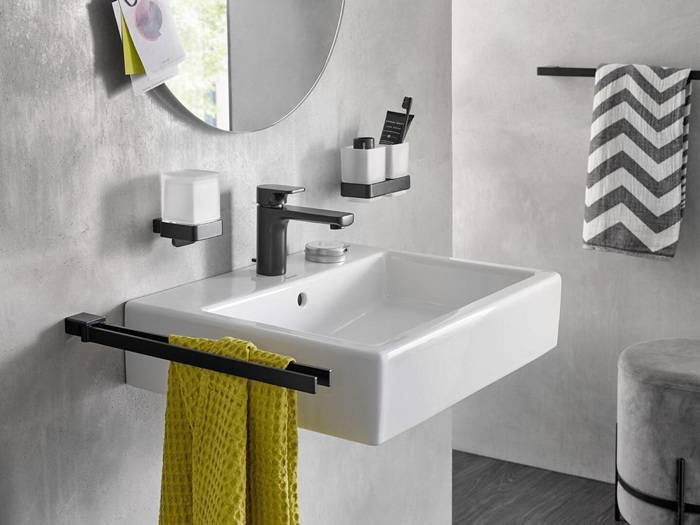 Ein modernes Waschbecken mit einem schwarzen Wasserhahn, einem Zahnbürstenhalter und einer Handtuchstange. Ein gelbes Handtuch hängt in der Nähe, und ein Spiegel befindet sich darüber.