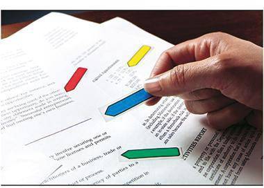 Eine Hand hält einen blauen pfeilförmigen Marker über einem Dokument mit farbigen Hervorhebungen, was auf eine Überprüfung oder Anmerkung von Text hinweist.