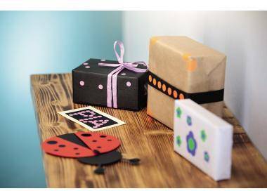 Handgefertigte Kunsthandwerk-Ausstellung auf einem Holztisch: eine Marienkäfer-Karte, eine dekorierte schwarze Geschenkbox, ein verpacktes Paket und eine gefaltete Karte.
