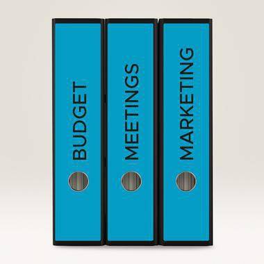 Drei blaue Aktenordner mit den Aufschriften „BUDGET", „MEETINGS"" und „MARKETING"" stehen aufrecht nebeneinander.