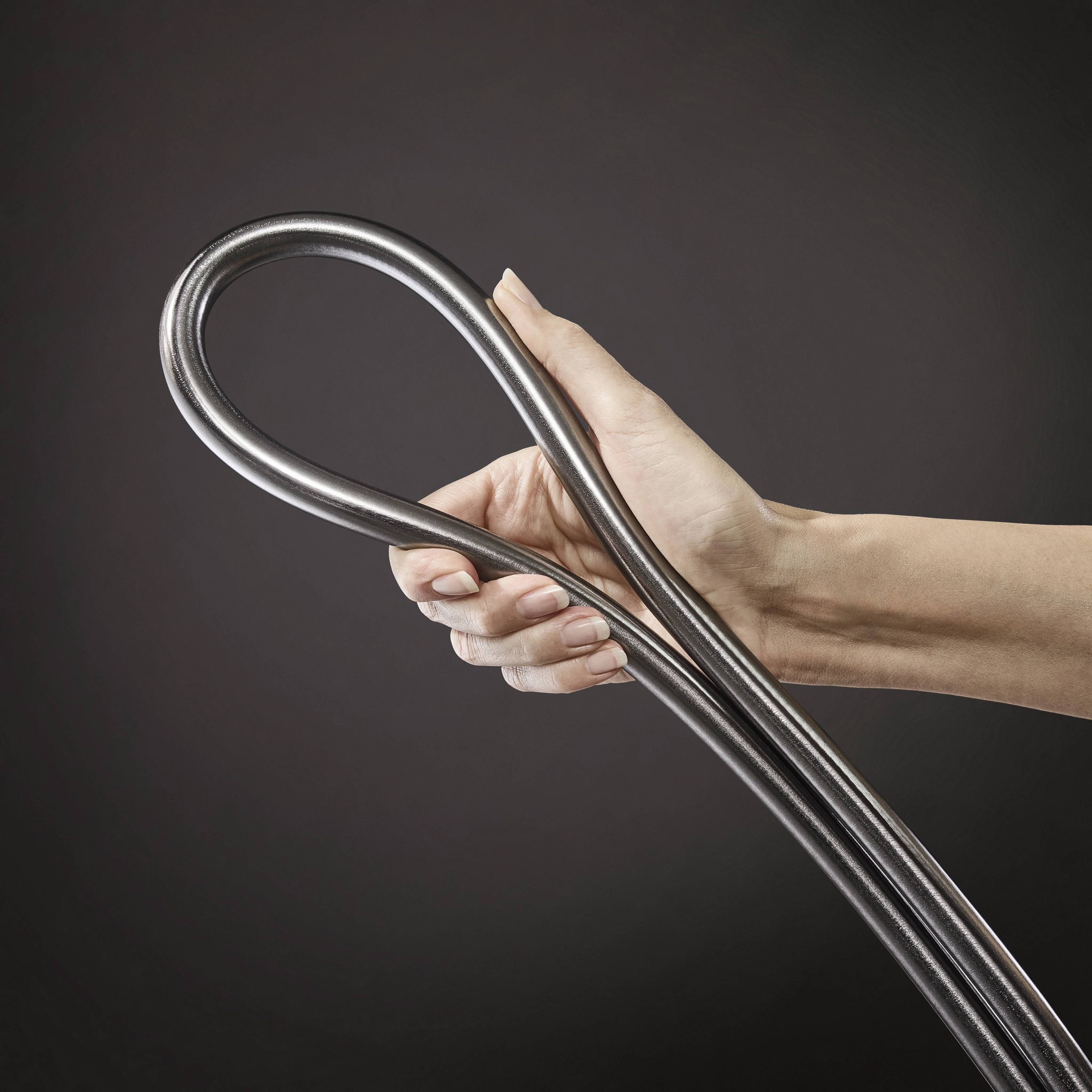 Nahaufnahme einer Hand, die ein flexibles Metallrohr gegen einen dunklen Hintergrund ergreift und biegt.