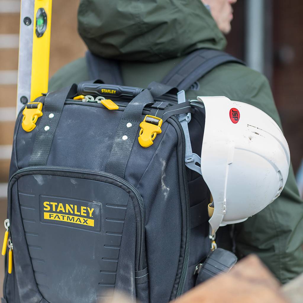 Bauarbeiter mit Schutzhelm und Stanley FatMax Werkzeugrucksack auf dem Rücken, mit einer Leiter dahinter.