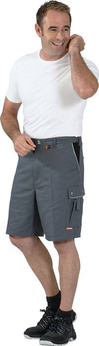 Lächelnder Mann, der ein weißes T-Shirt und graue Shorts trägt, posiert mit einer Hand in der Nähe seines Ohrs und der anderen in seiner Tasche.