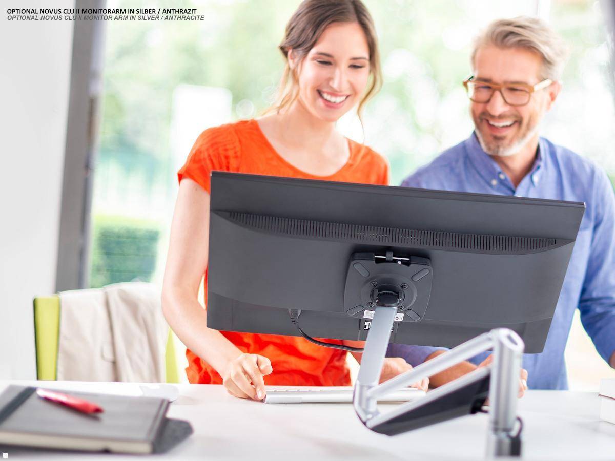 Zwei Personen, die lächelnd auf einen Computermonitor auf einem Schreibtisch blicken und gemeinsam in einer hellen Büroumgebung arbeiten.