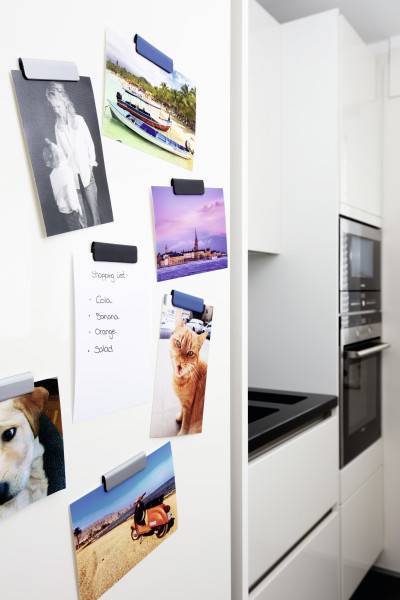Weißer Kühlschrank, der als Fotoanzeige verwendet wird, mit geklammertem Schnappschüssen, einem Notizzettel mit den Einträgen 'Groza', 'Donna', 'Orange' und 'Słodki', neben einem modernen Einbauofen.