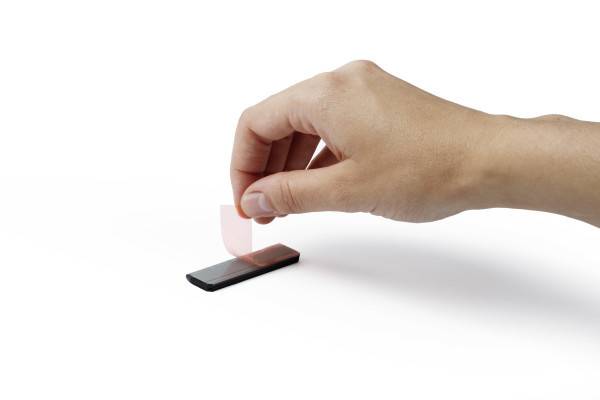 Hand, die eine kleine durchsichtige rote Karte auf ein schwarzes Smartphone auf weißem Hintergrund legt.