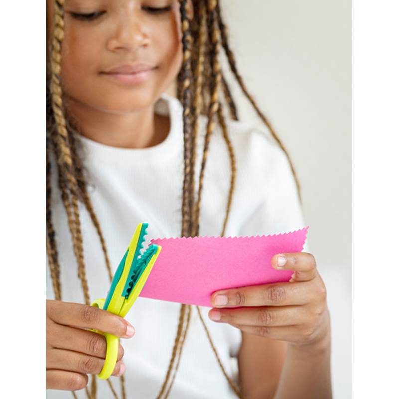 Ein Kind verwendet gemusterte Schere, um ein rosafarbenes Stück Papier zu schneiden, konzentriert auf die Aktivität, wobei Kreativität und handwerkliche Fähigkeiten hervorgehoben werden.