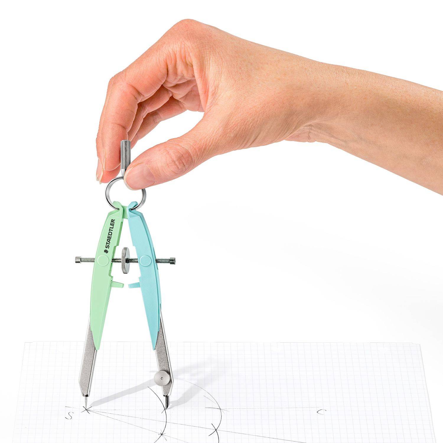 Hand, die einen Zirkel über Millimeterpapier hält, zeichnet einen Kreis und Bögen auf einer technischen Skizze.