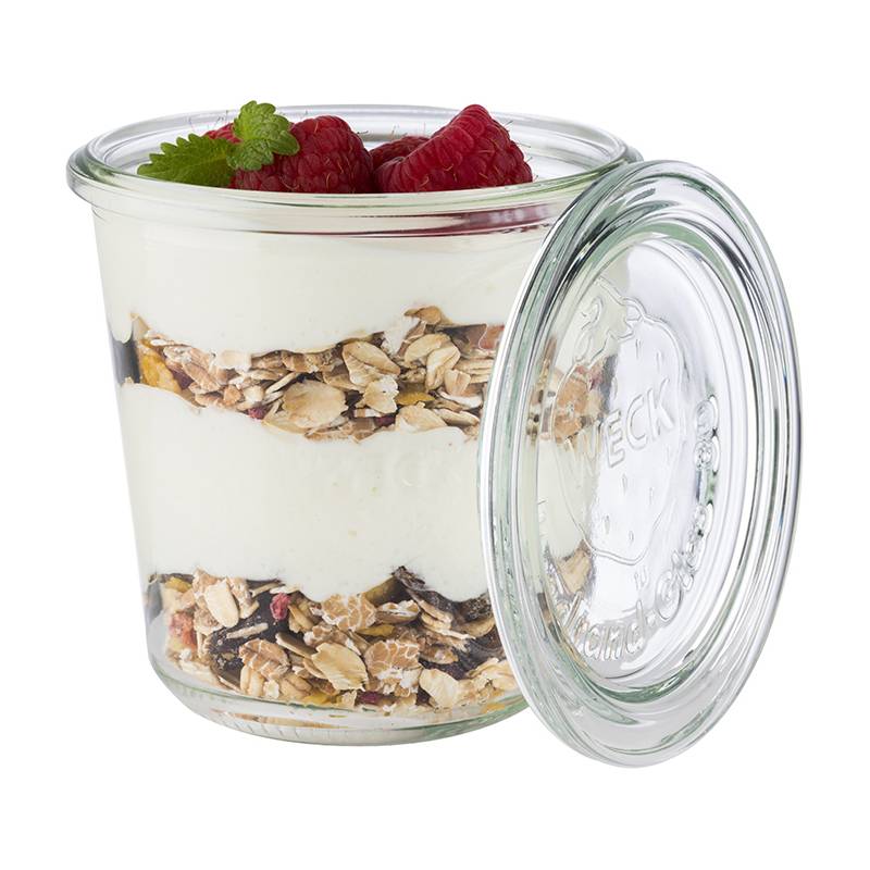 Ein Glasgefäß mit Schichten aus Joghurt, Granola und Himbeeren obenauf, garniert mit einem Minzblatt.