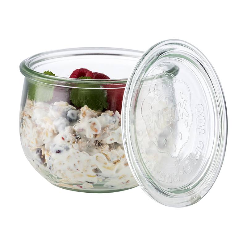 Ein Glasglas gefüllt mit Müsli, das mit Joghurt vermischt ist, und obenauf frische Himbeeren und Minzblätter. Der Deckel des Glases ist teilweise geöffnet.