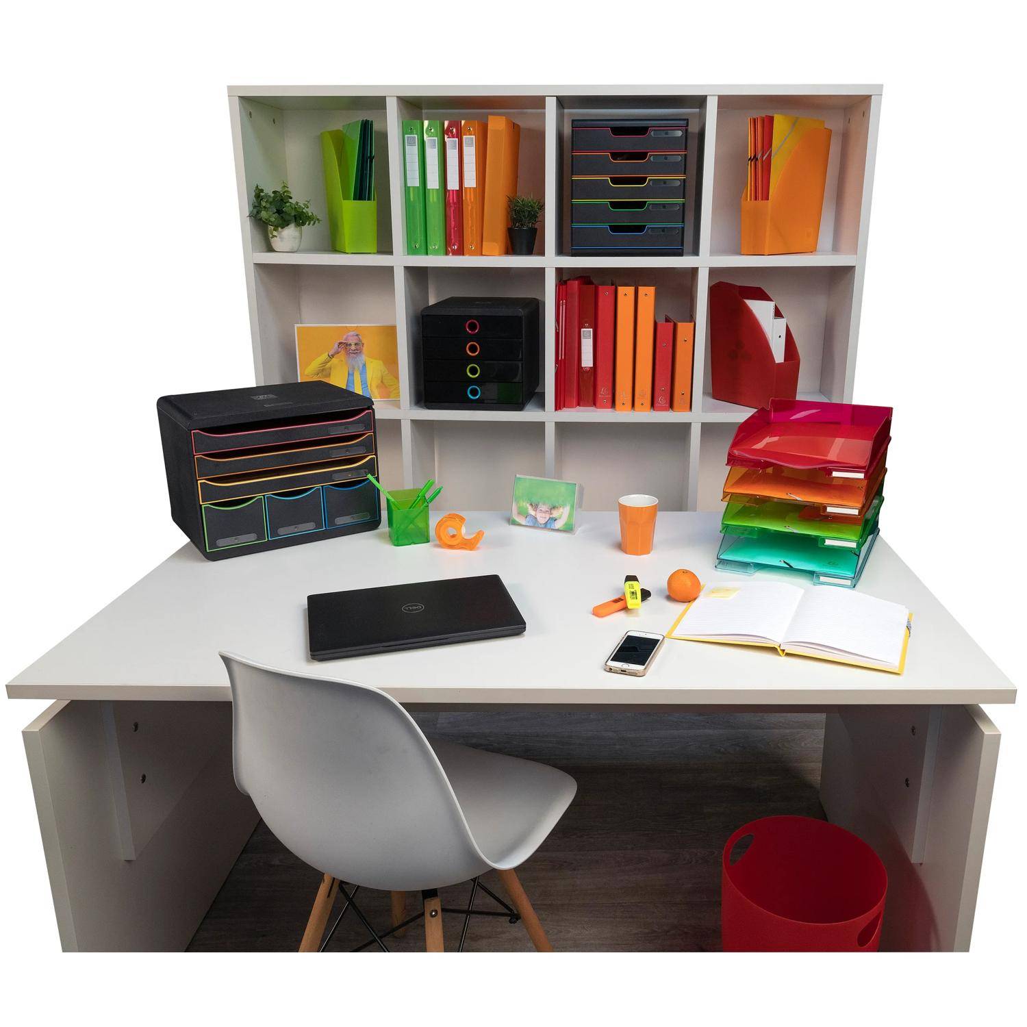 Organisierter Schreibtisch mit einem Stuhl, Laptop, offenem Notizbuch, Telefon und farbigen Ablagefächern vor einem Fachbodensystem, das mit Ordnern und Büromaterialien gefüllt ist.
