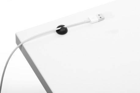 Weißes USB-Kabel, das durch eine schwarze Kabelöse am Rand eines weißen Schreibtischs oder einer weißen Tischplatte verläuft.