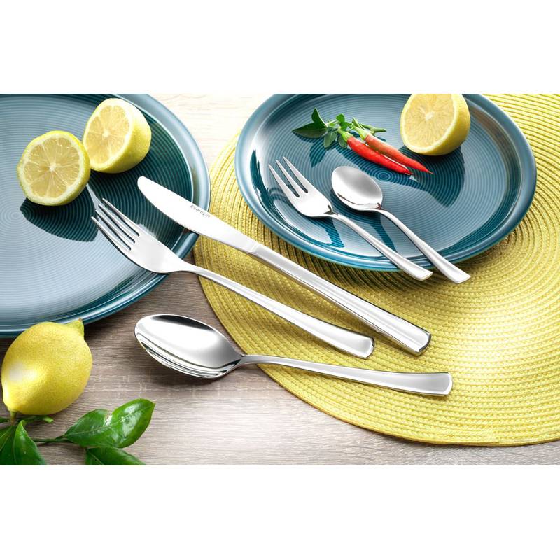 Eine Tischdecke mit zwei blauen Tellern, auf denen jeweils Besteck liegt. Auf einem Teller sind Zitronenscheiben verteilt, auf dem anderen ein ganzer Zitrone, Kräuter und rote Chilischoten.