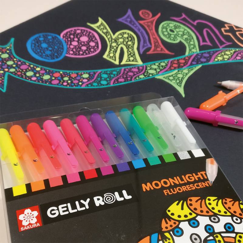 Das Bild zeigt einen Satz Gelly Roll Moonlight Leuchtfarben-Stifte auf schwarzem Papier, mit leuchtend bunten Farben und einem Doodle des Wortes 