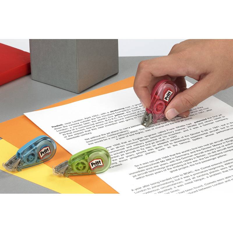 Eine Hand benutzt einen roten Korrekturbanddrucker auf einem gedruckten Dokument. Blaue und grüne Spender liegen auf dem Papier und zeigen Text darunter.