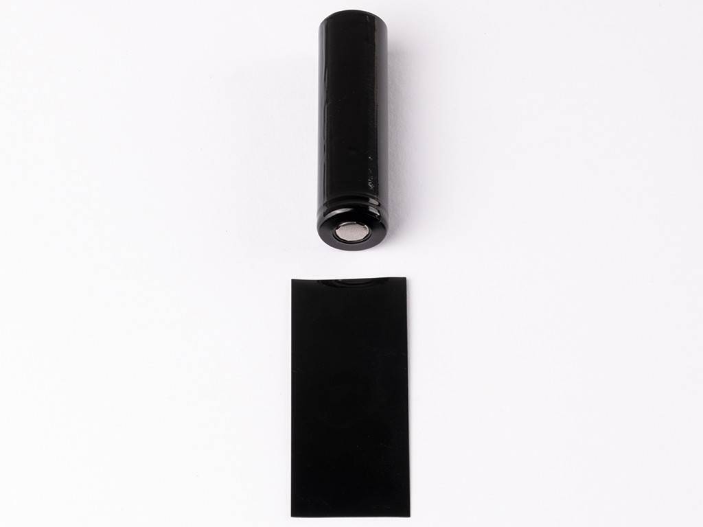 Schwarze zylindrische Batterie über einer flachen schwarzen rechteckigen Karte, beide isoliert auf weißem Hintergrund.