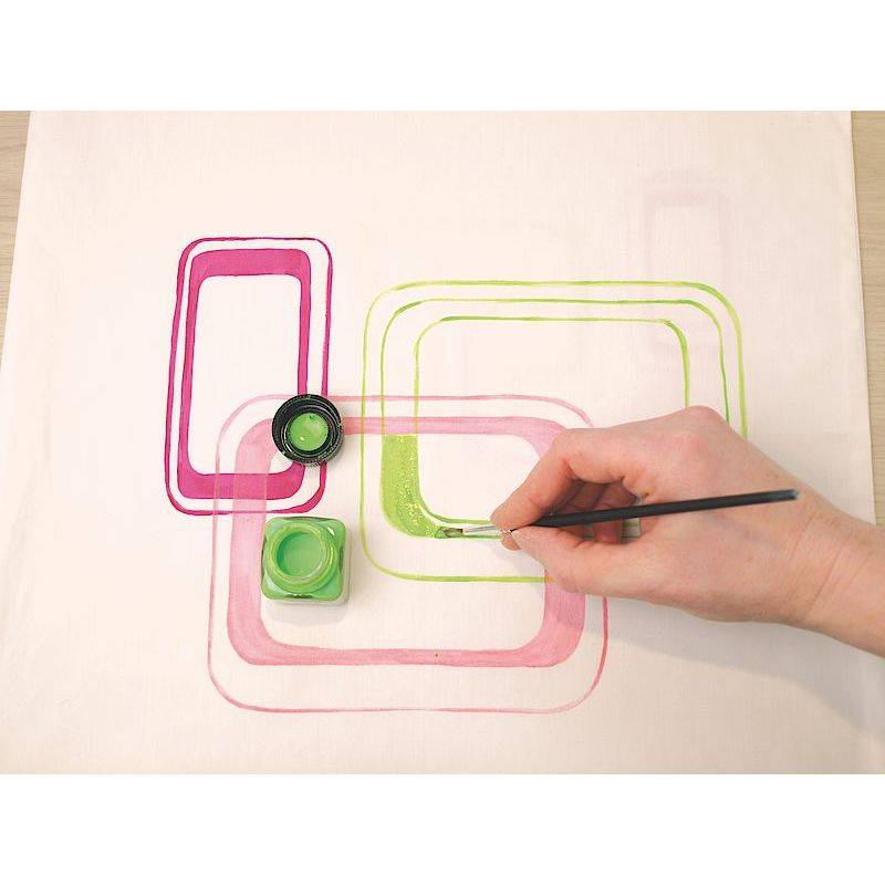 Eine Hand malt sich überlappende rosa und grüne rechteckige Muster auf eine weiße Leinwand, wobei sie einen feinen Pinsel und ein offenes grünes Farbglas verwendet.