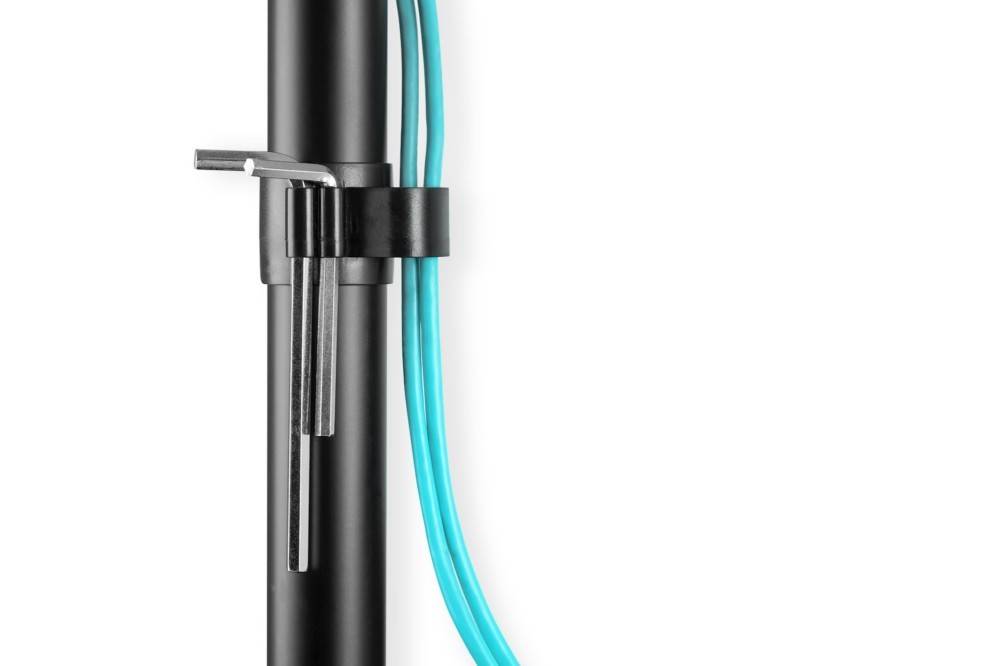 Nahaufnahme eines vertikalen schwarzen Metallstabs mit einem U-förmigen Griff, der durch eine Klemme befestigt ist. Blaue Kabel verlaufen parallel an der Seite des Stabs.