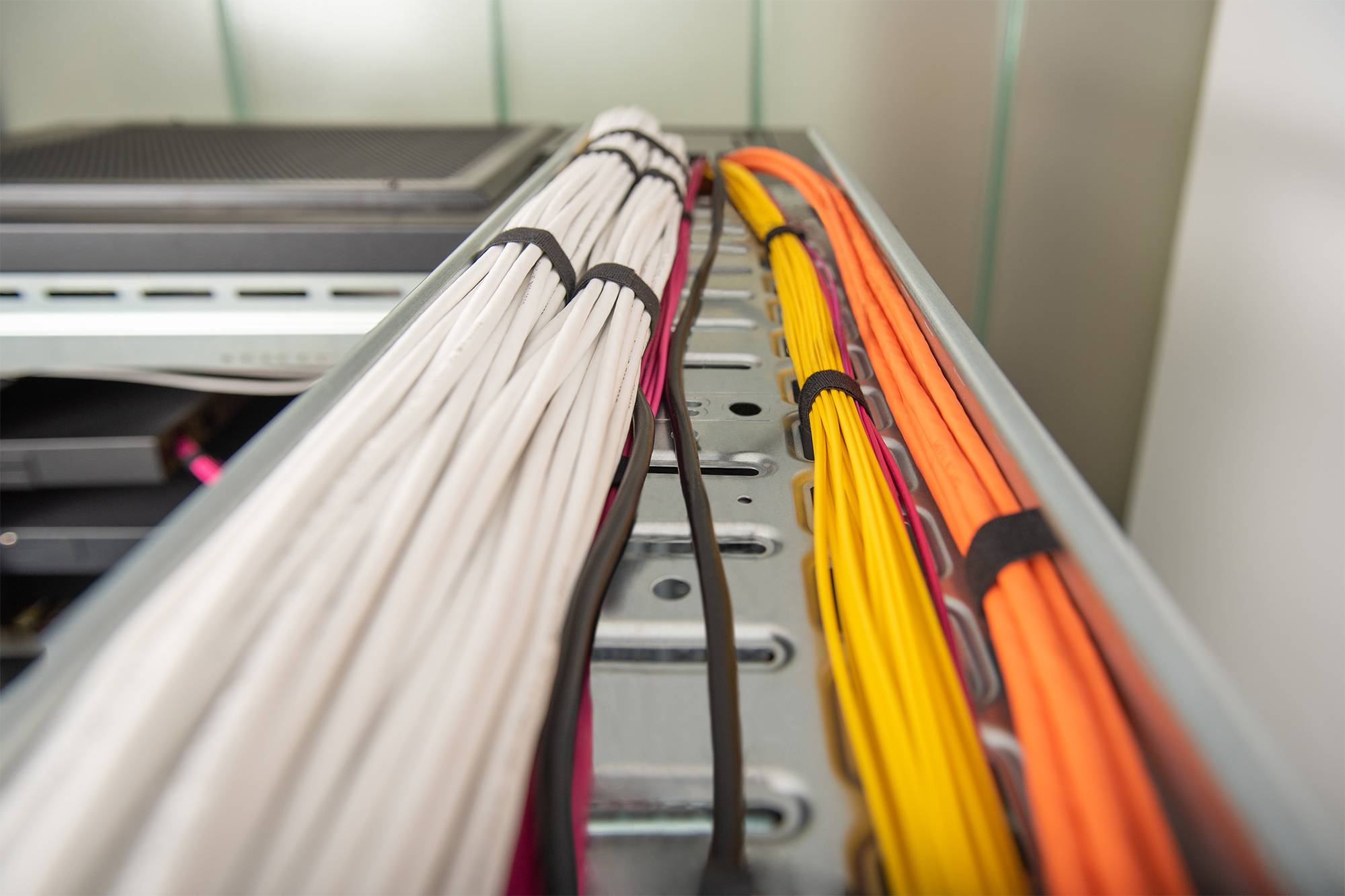 Farblich gekennzeichnete Netzwerkkabel, ordentlich gebündelt und durch ein Serverrack oder eine Kabelführungsschiene geleitet.