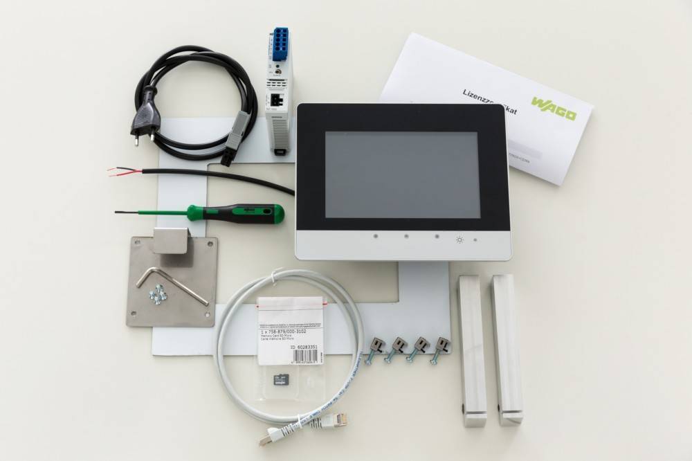 Ein elektronisches Set mit einem Monitor, Kabeln, Anschlüssen und Werkzeugen. Enthält einen Schlitzschraubendreher, Schrauben und ein Lizenzierungsdokument.