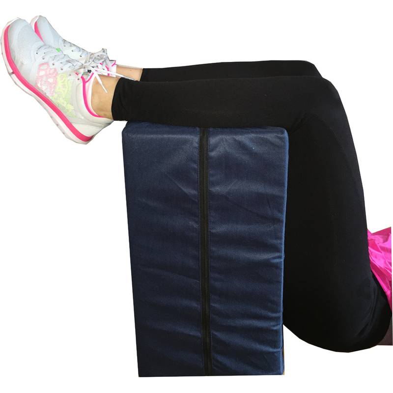 Eine Person trägt Leggings und Turnschuhe und liegt mit erhöhten Beinen auf einem großen Kissen, möglicherweise zur Entspannung oder zur Unterstützung beim Training.