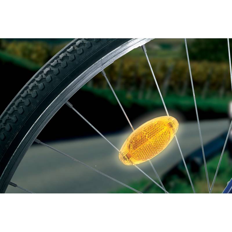 Ein Fahrradrad mit einem gelben Reflektor, der an einer Speiche befestigt ist, neben einer Landstraße und verschwommener Vegetation im Hintergrund.