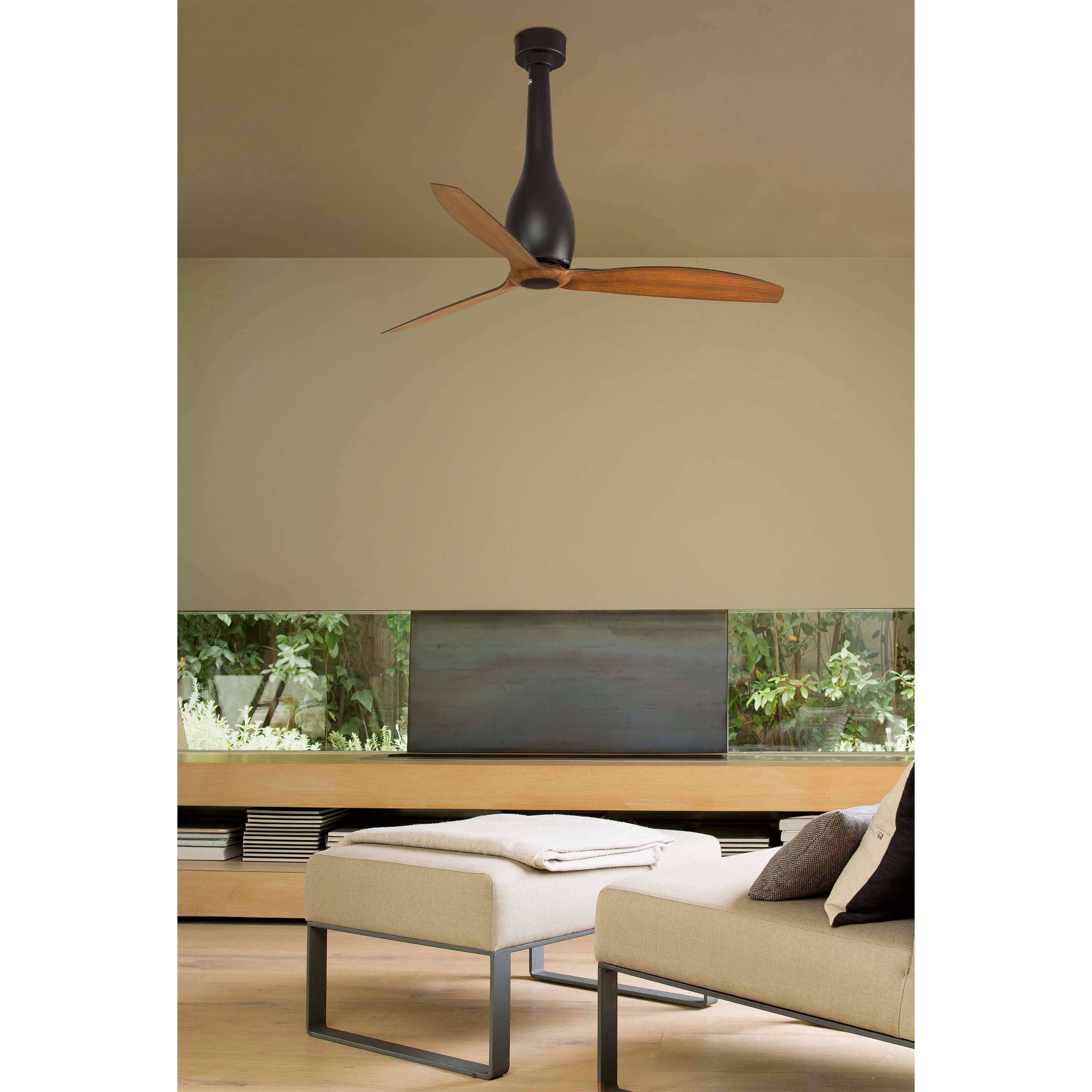 Deckenlüfter mit Holzflügeln über einem modernen Wohnzimmer mit einer beigen Couch, gepolstertem Hocker und Blick auf Grünflächen durch große Fenster.