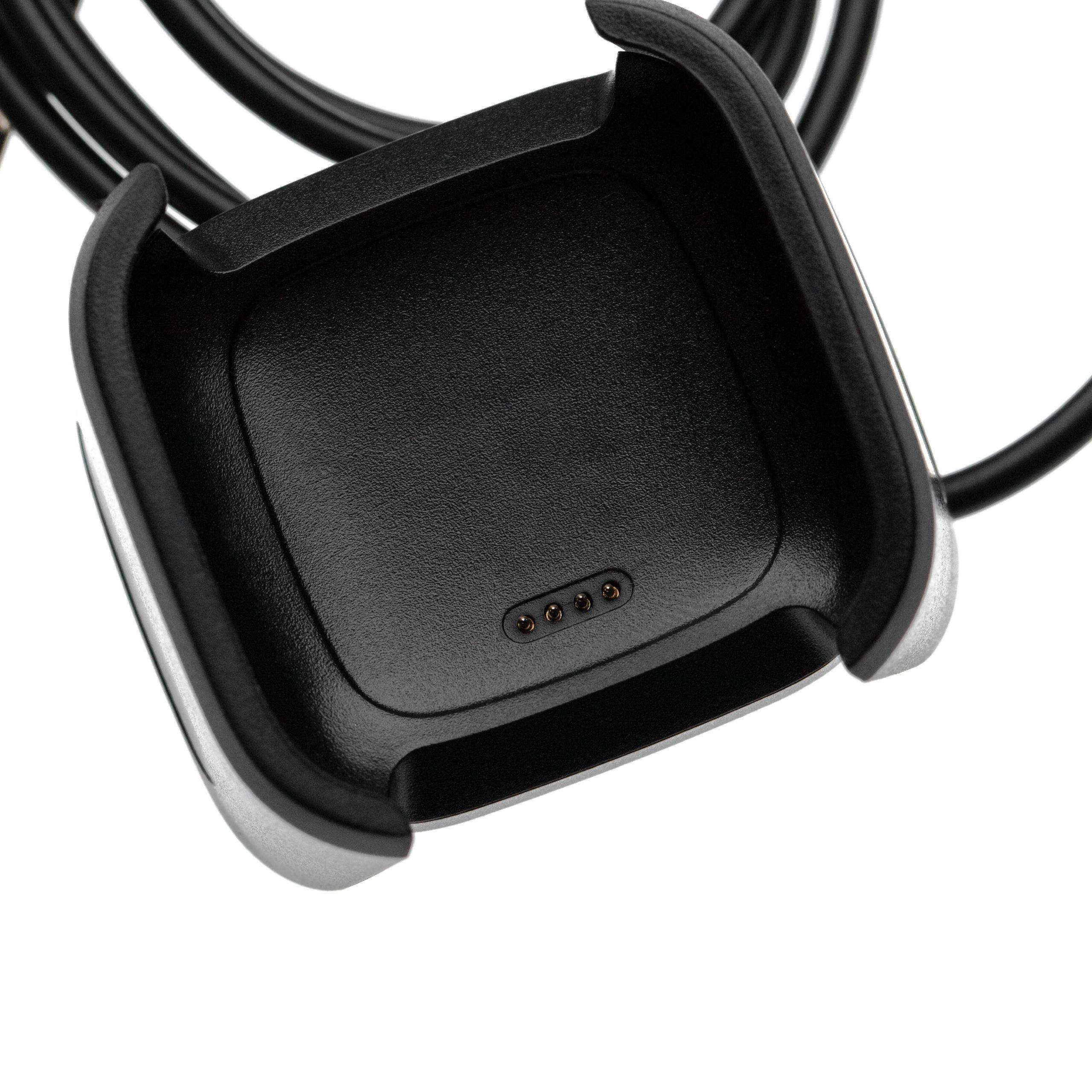 Nahaufnahme einer schwarzen Smartwatch-Ladewiege mit vier Metallkontakten und angekabeltem Kabel auf weißem Hintergrund.