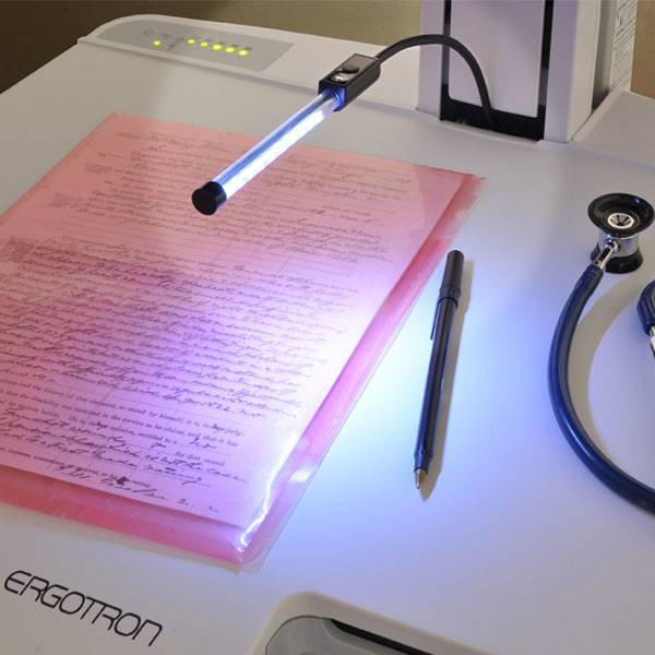 Ein Dokumentenscanner mit einer rosa gefärbten Seite unter einer blauen Lichtleiste, daneben ein Stift und ein Stethoskop auf einem weißen Schreibtisch.