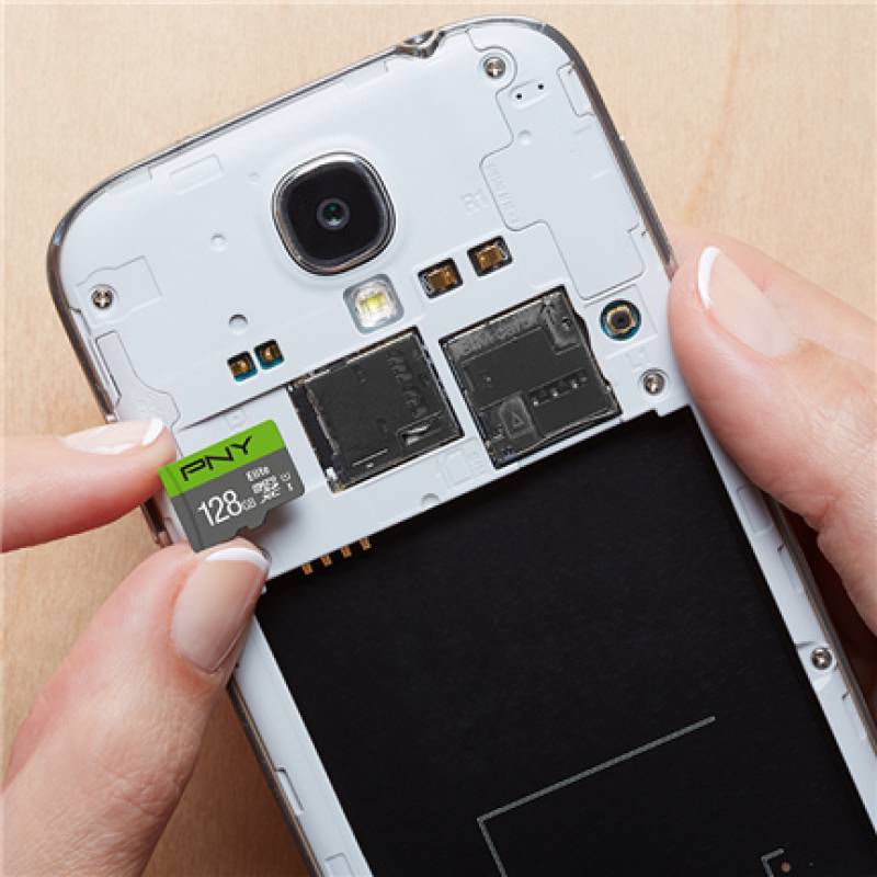 Hände führen eine 128GB-Mikro-SD-Karte in die Rückseite eines Smartphones mit entfernter Abdeckung ein und zeigen interne Komponenten und Kamera.