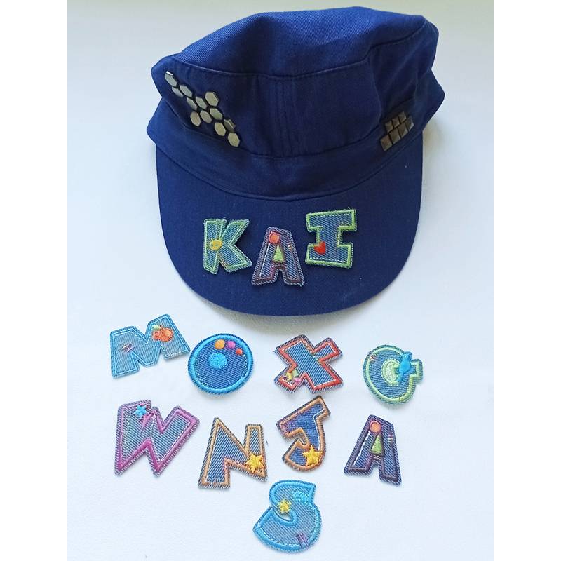 Blaue Kappe mit geometrischen Designs auf der Vorderseite. Darunter bilden farbenfrohe, bestickte Buchstaben und Symbole einen Namen und erschaffen ein verspieltes Muster.