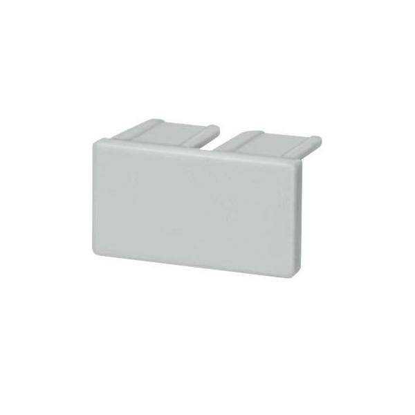 Ein kleines, rechteckiges, hellgraues Plastikbauteil mit zwei hervorstehenden Laschen oben, möglicherweise eine Anschlussabdeckung oder Kappe.