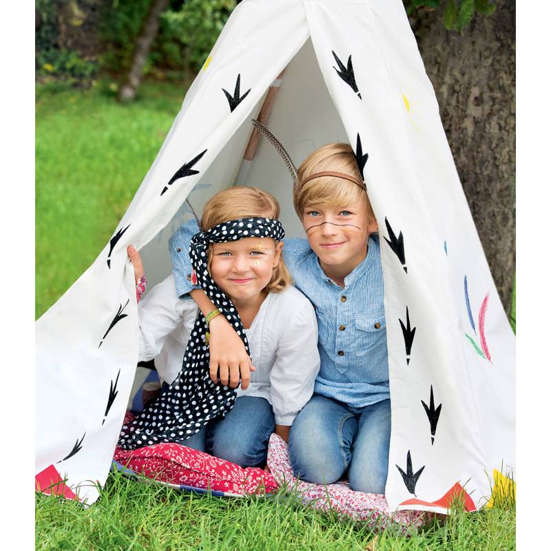 Zwei Kinder sitzen in einem kleinen Tipi auf Gras. Sie tragen Gesichtsbemalung und lässige Kleidung und lächeln fröhlich im Freien.