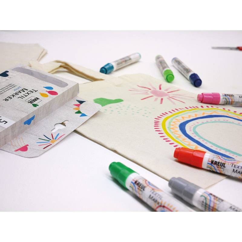 Stoff mit bunten Mustern bemalt, die mit Markern gestaltet wurden, umgeben von verschiedenfarbigen Markern und Verpackungen auf einer weißen Oberfläche.