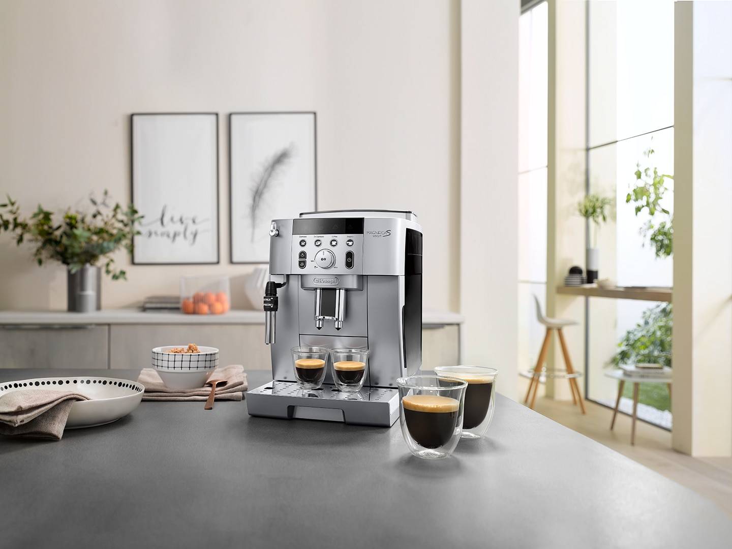 Edelstahlespressomaschine, die zwei kleine Tassen Kaffee auf einer Küchentheke braut, mit zwei gefüllten Glastassen davor.