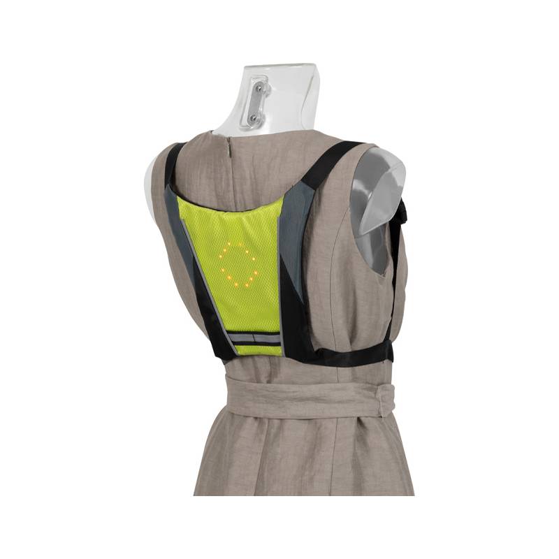 Eine Schaufensterpuppe trägt ein beiges Kleid und eine limettenfarbene Sicherheitsweste mit einer LED-Anzeige auf dem Rücken, die ein Linksabbiegen signalisiert.