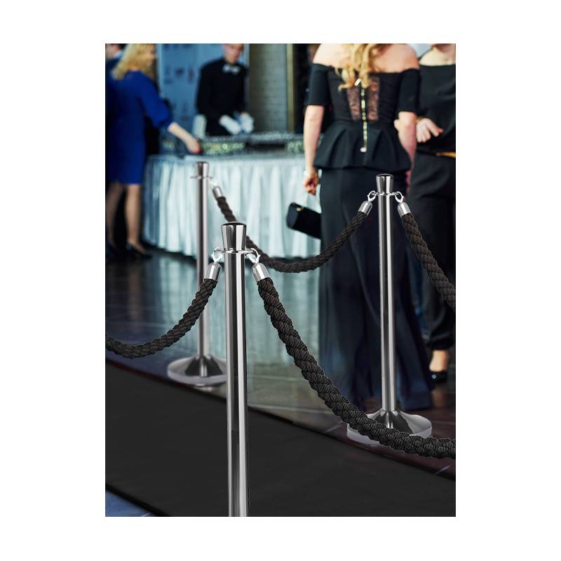 Absperrständer mit schwarzen Seilen bilden eine Barriere bei einer Veranstaltung, während im Hintergrund Menschen formell gekleidet sind, was auf eine Gala oder eine VIP-Veranstaltung hindeutet.