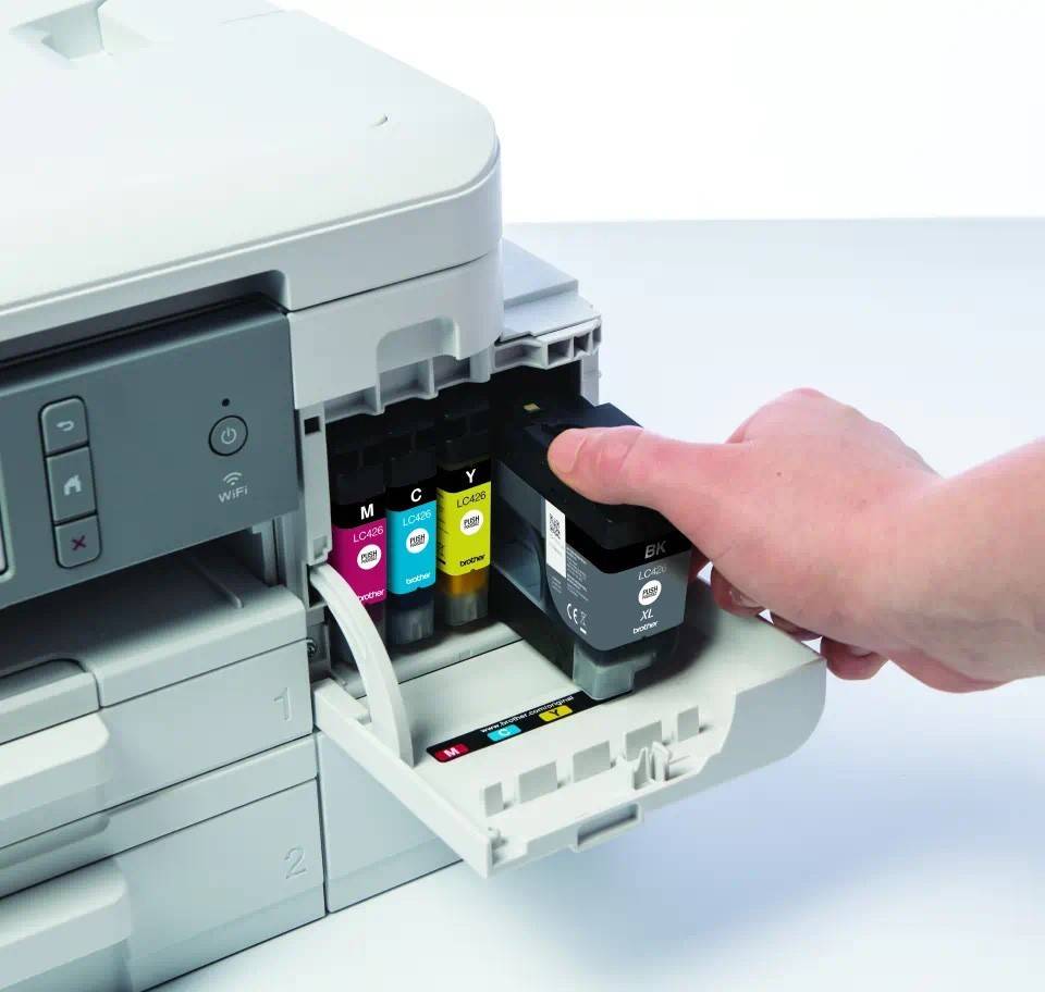 Eine Hand ersetzt eine schwarze Tintenpatrone in einem Farbdrucker, wobei die Cyan-, Magenta- und Gelb-Patronen sichtbar sind.