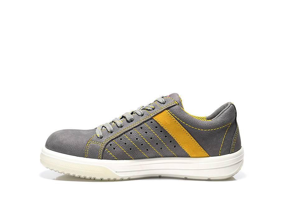 Ein grauer Sneaker mit gelben Akzenten und weißer Sohle, mit grauen Schnürsenkeln und Stickdetails, von der Seite auf weißem Hintergrund betrachtet.